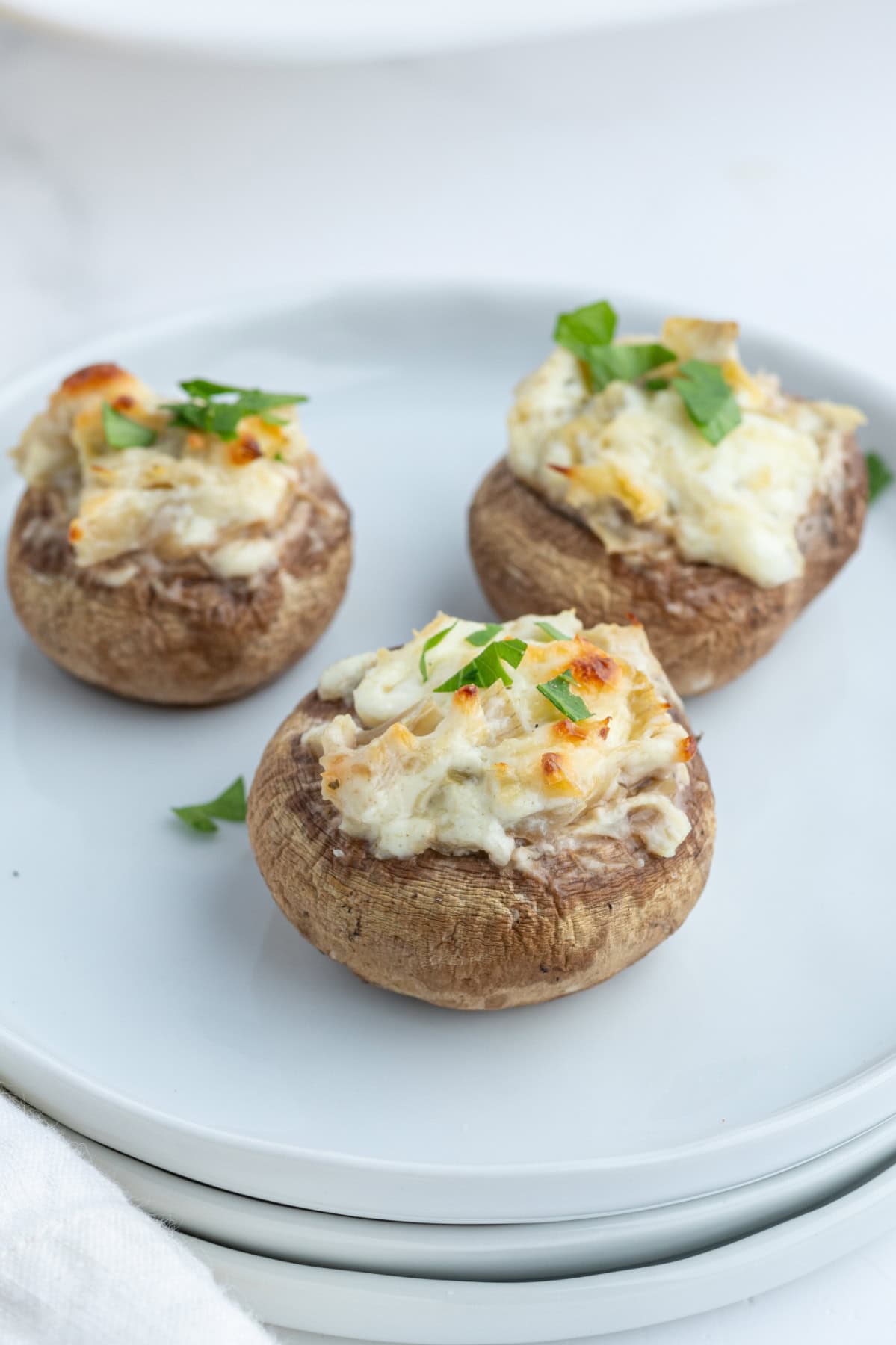 Artichoke Stuffed Mushrooms recipe from RecipeGirl.com three artichoke stuffed mushrooms on plate