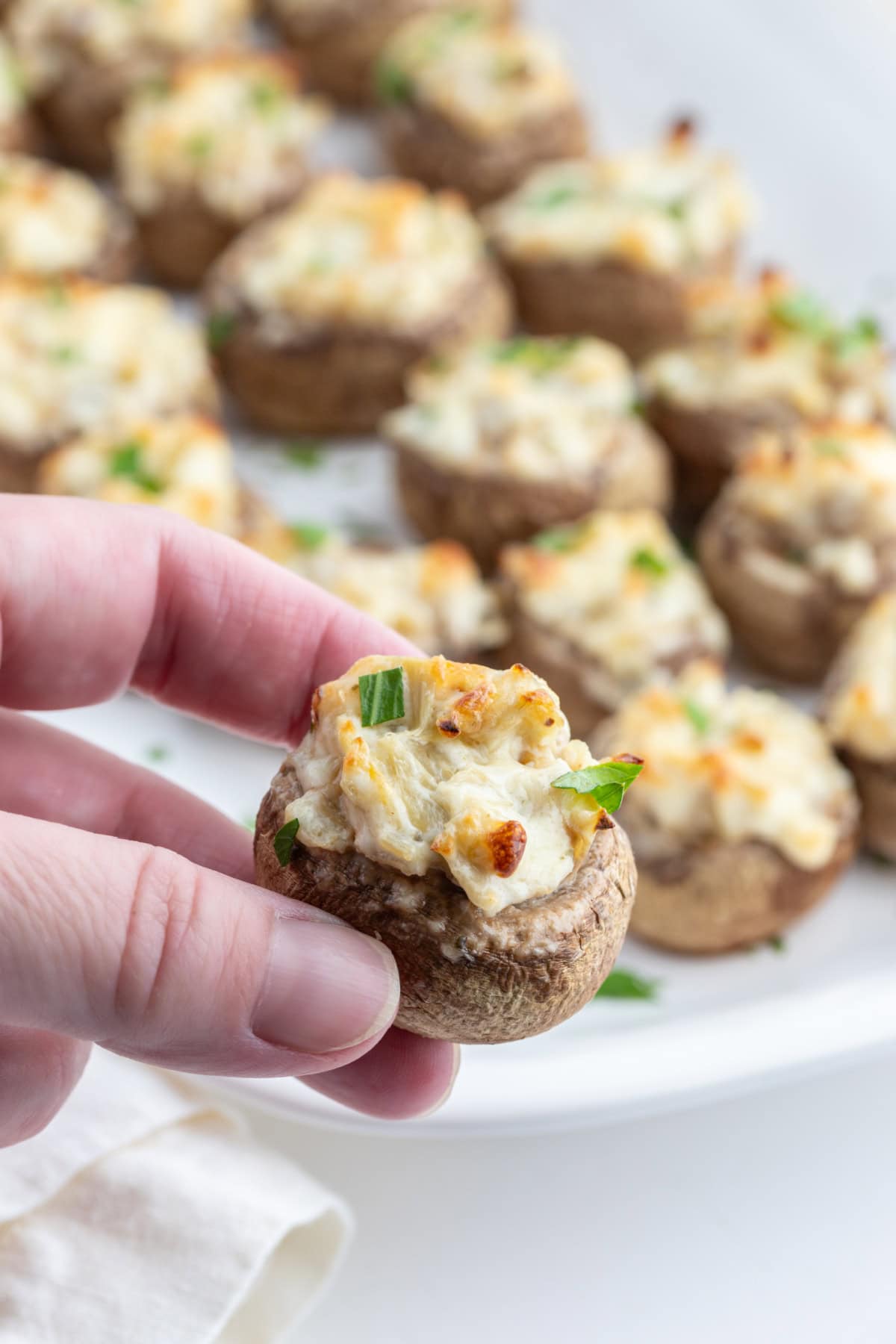Artichoke Stuffed Mushrooms recipe from RecipeGirl.com hand holding artichoke stuffed mushroom