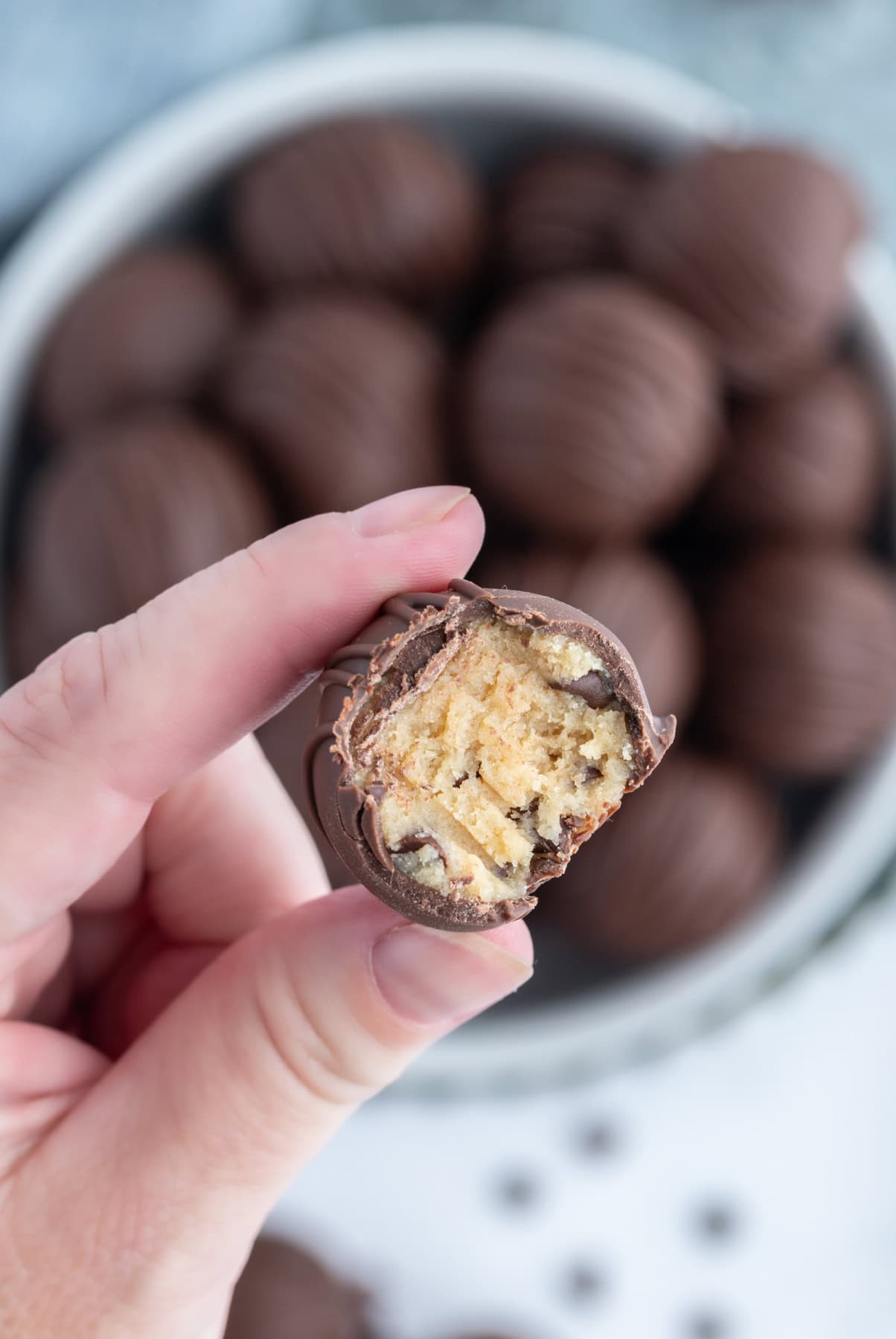 Chocolate Chip Cookie Dough Truffles recipe from RecipeGirl.com flour safe to eat : chocolate covered chocolate chip cookie dough lovers fingers holding a chocolate chip cookie dough truffle with bite taken out