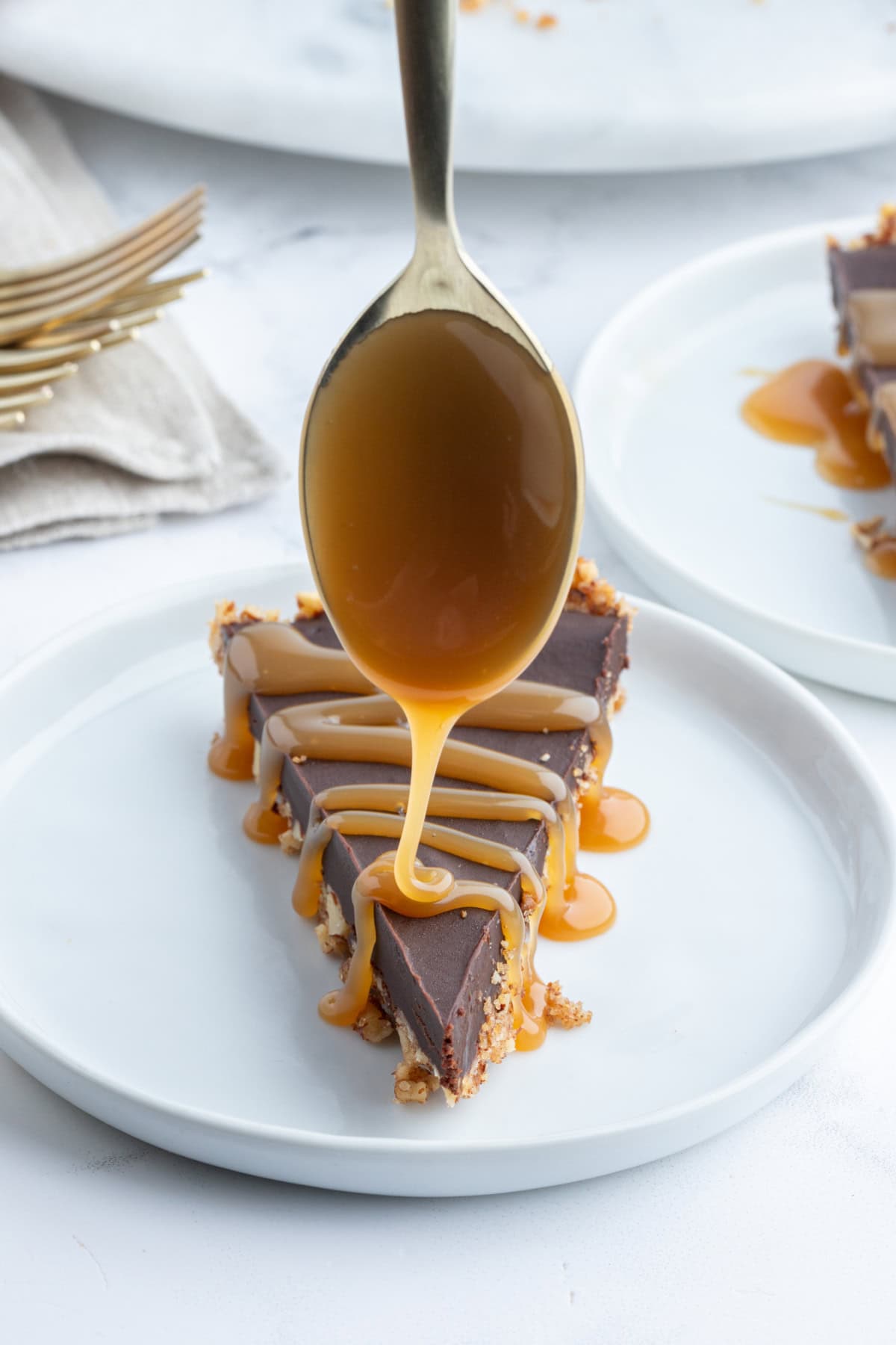 Chocolate Pecan Tart with Caramel Sauce recipe from RecipeGirl.com spooning caramel sauce on top of slice of chocolate pecan tart on plate