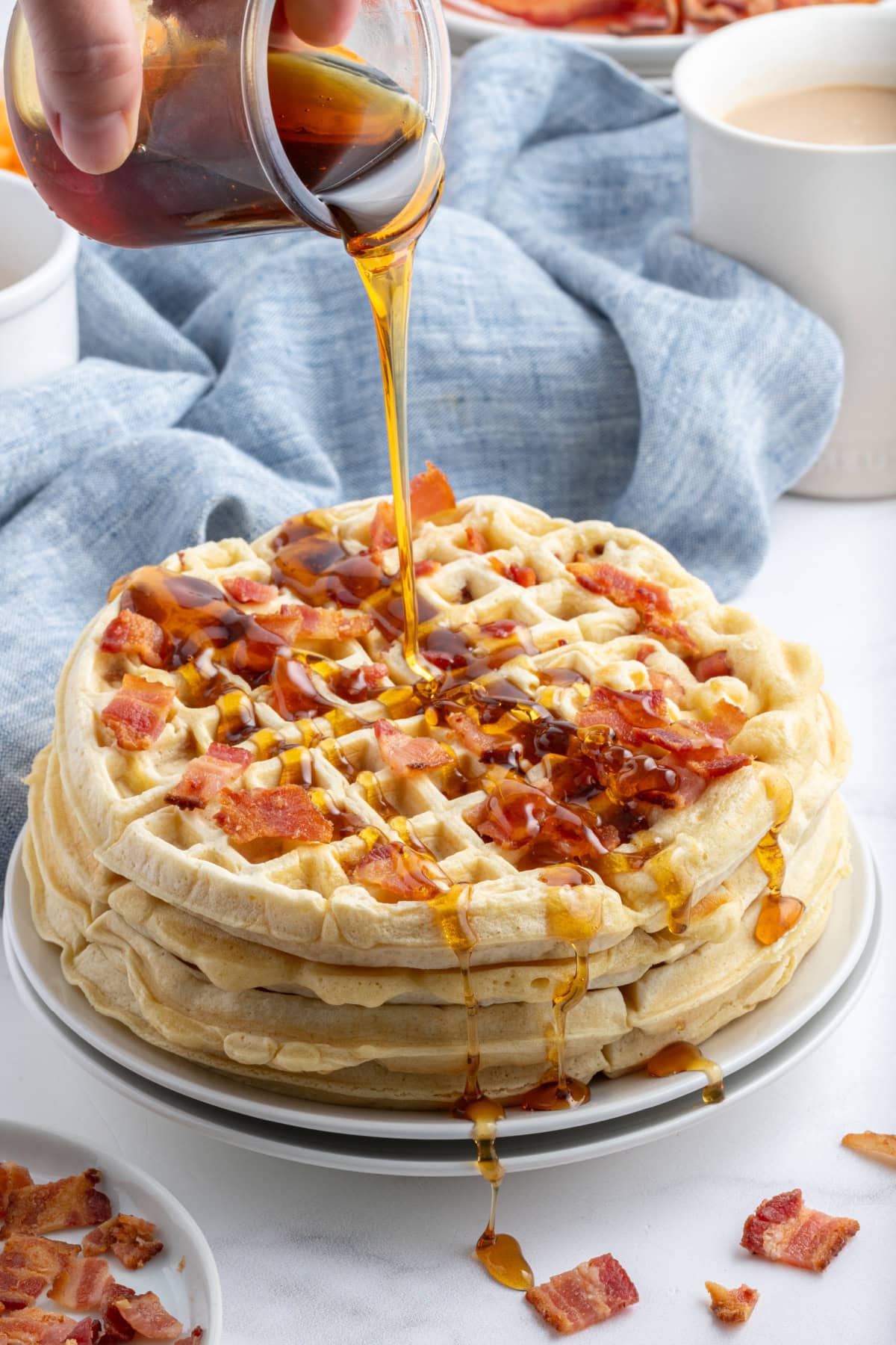 Maple Bacon Waffles recipe from RecipeGirl.com pouring syrup onto stack of maple bacon waffles