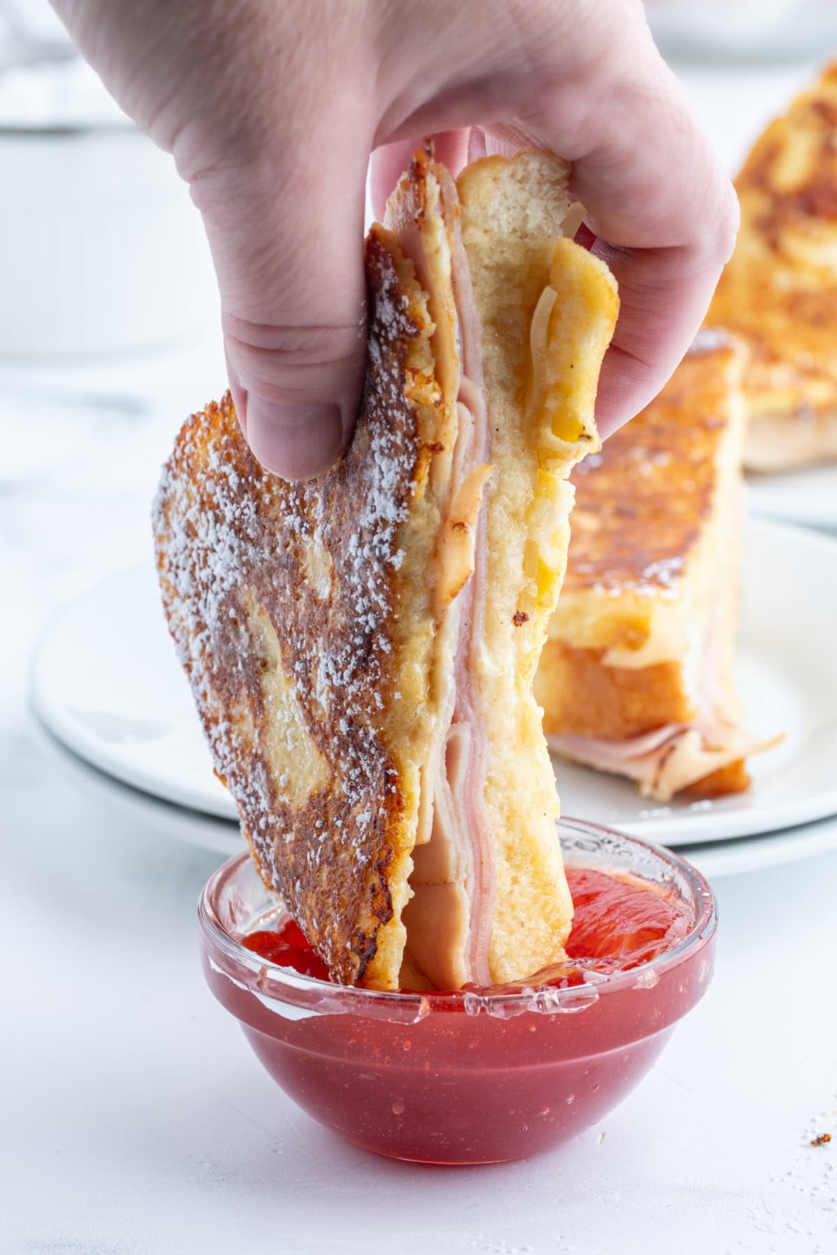 Monte Cristo Sandwich : classic French recipe from RecipeGirl.com dipping monte cristo sandwich halve in jam