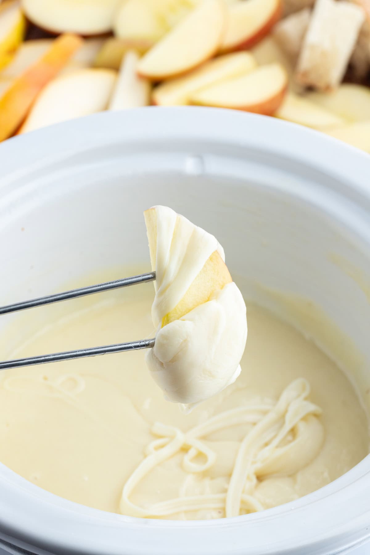 Classic Swiss Fondue recipe from RecipeGirl.com fork holding apple slice that has just been dunked into swiss cheese fondue